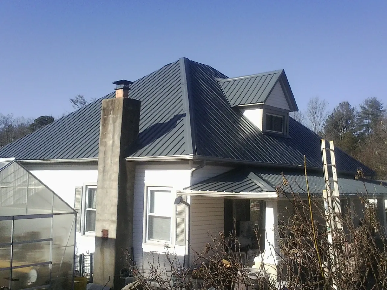 Dark blue standing seam metal roof on a white farmhouse with dormer — Slate & Tile Roof Repair by Roofing Brothers in Mirror Lake