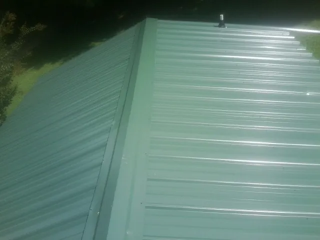New green metal panels meeting at the ridge of a roof — Flat Roof Repair work by our crew in Mirror Lake