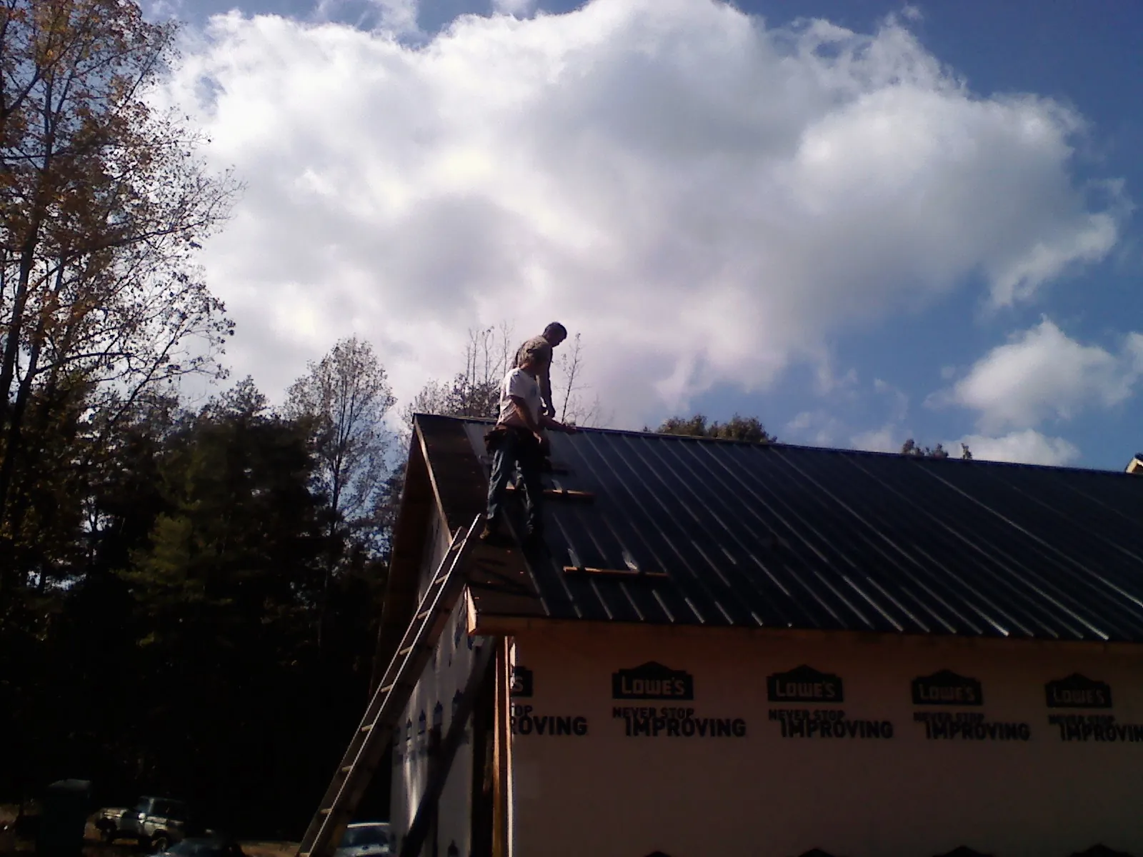 Roofer fastening dark metal panels high against a cloudy sky, from a Roof Inspection job in Mirror Lake