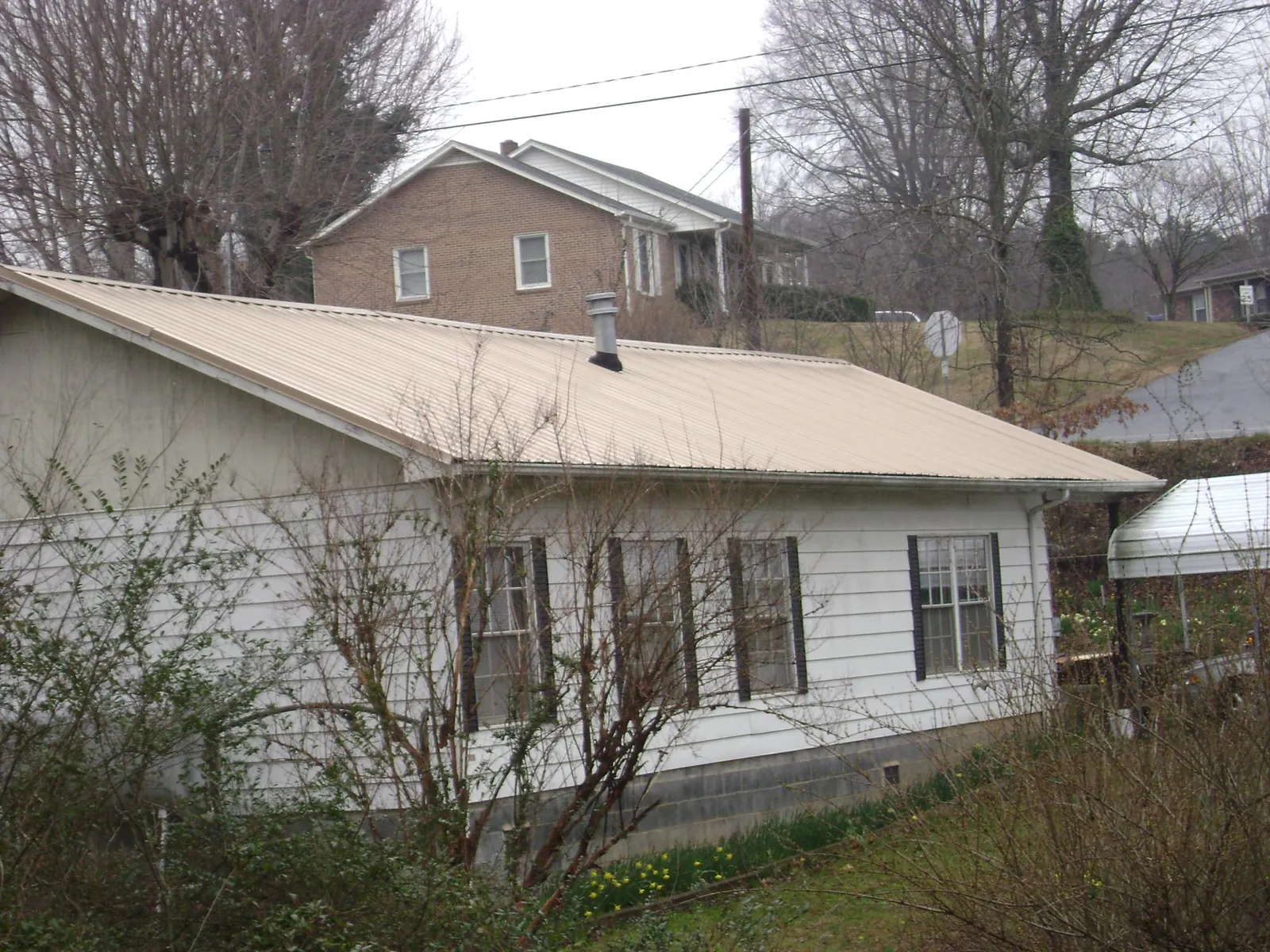 Tan metal roof on a white sided house set into a hillside — Commercial Roofing by Roofing Brothers in Mirror Lake